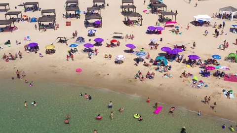 Dor, Israel - July 4, 2020: Crowded public beach with colourful umbrellas and people in the water and relaxing on the sand, Aerial view.