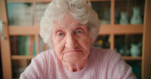 Close-up face of a sad old woman with deep wrinkles winking her eyes.