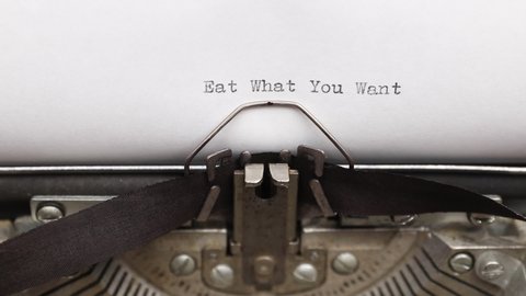 Typing a phrase Eat What You Want Day on a vintage typewriter close-up. concept of festive banner for national holiday