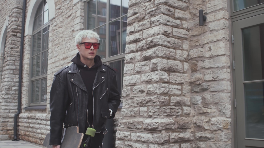 Portrait of stylish teenage young guy riding on the skateboard outdoor. Teenager with a skate board on the street. Sport and subculture.