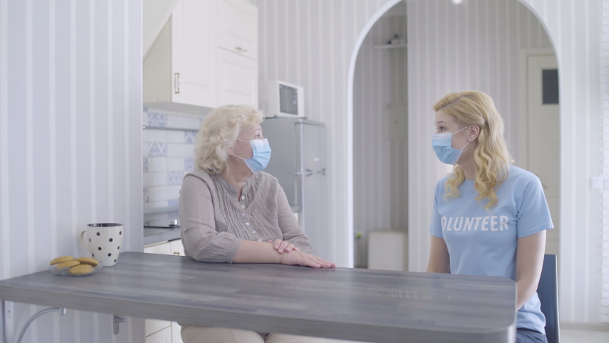 Female volunteer visiting senior woman at home, wearing face mask for protection Royalty-Free Stock Footage #1055433566
