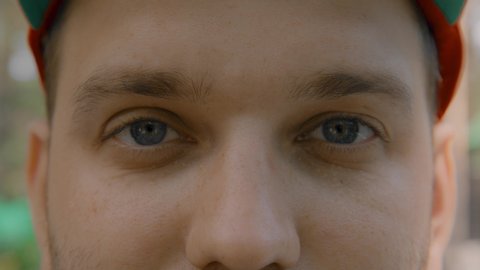 Close-up portrait of a young man. Blue eyes of a young guy close-up, natural beauty. The young guy looks at the camera, blinks, and smiles. Full-face view. Warm color, slow motion. 4K