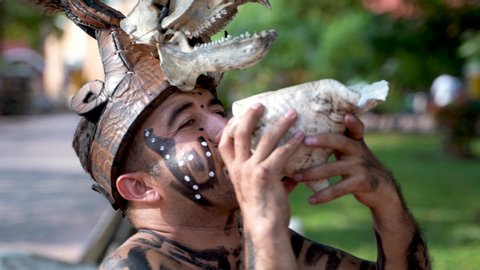 Closeup of a Mayan or Aztec dancer musician blowing into a conch shell as part of a sacred dance performance in Valladolid, Mexico.