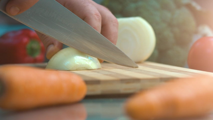 The chef uses a kitchen knife to cut the white onion in a thin slice on a wooden chopping block.The Chef Uses A Kitchen Knife To Slice A White Onion Royalty-Free Stock Footage #1055436092