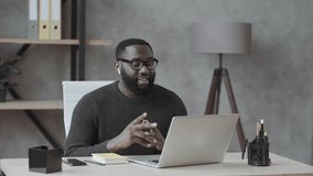 black guy waves his hand into a laptop and communicates via video link in casual clothes at home, office