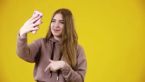 Portrait of cheerful blogger holding cell phone making video call or doing blog online isolated on yellow background 