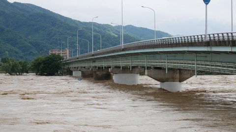 Flooding in Yatsushiro, Japan. Heavy rain caused the Kuma River to overflow and flood the city. Debris floats down the raging high waters that are nearly flowing over a bridge.