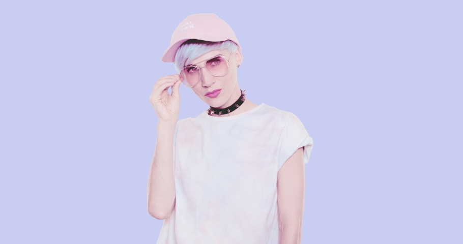 Fashion alternative Girl with blue hair and stylish summer look sunglasses and cap posing in studio against blue background. Fashion accessories concept