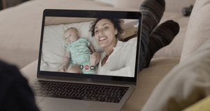 Mother and her newborn baby in bed making video call to family member on sofa using laptop