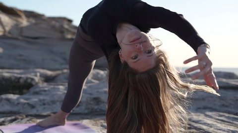Female doing Yoga on an Ocean Cliff at Sunrise. Shot in Australia on beach cliff, with ocean waves beneath. Shot details: close up of female in workout exhaling and relaxing, inverted yoga pose.