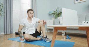 An athletic fitness instructor speaking on a labtop webcam streaming online training lessons. A muscular sportsman talking to his followers on gymnastics, athletics. Home workout, social distance.