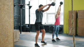Slow motion of young couple guy and girl exercising in gym squatting with kettlebells working out together. Crossfit, active lifestyle and people concept. - Powered by Shutterstock - Get 15% off with code: PIKWIZARD15