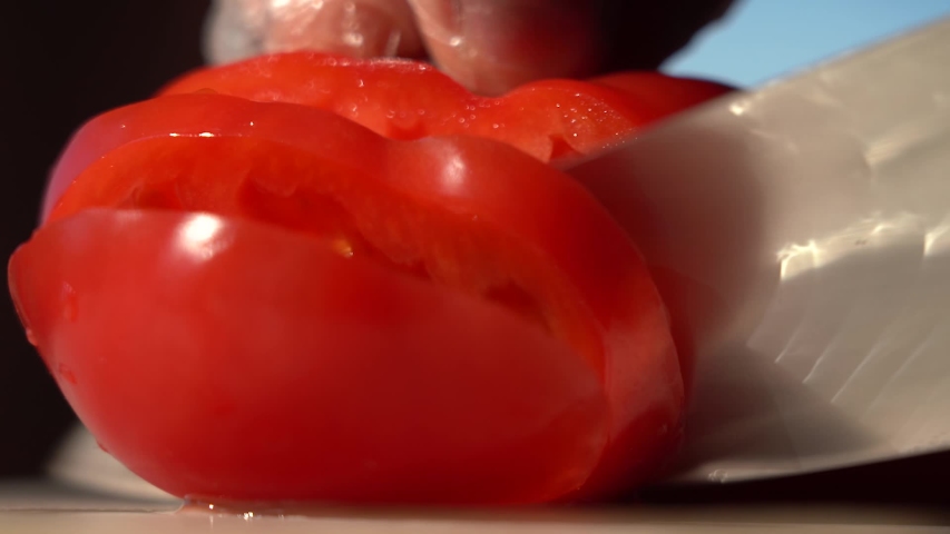 Cut Red Tomato in the morning light. Cut fresh vegetables for cooking in the morning light. Macro. Tomato cutting close up. Natural sunlight. Cook's hands in gloves.