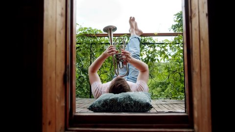 a happy man plays the trumpet on the balcony. feet up free time for a favorite activity in the midst of a coronavirus pandemic and social distancing