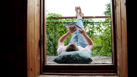 a man lies on his balcony and reads a book with his legs up. social distance during the coronavirus pandemic. time to get smarter