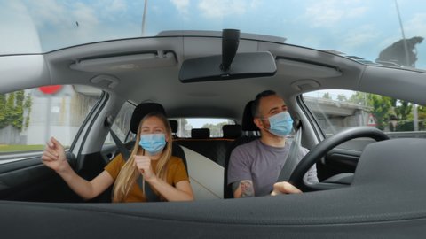Happy young couple, friends finally go on vacation after quarantine and lockdown due to corona virus. Excited dance inside car on road trip in new normal, in face masks. Safe staycation concept