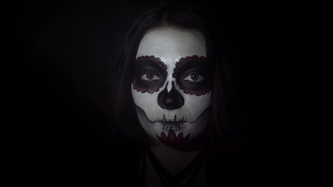 Portrait of a girl with traditional Santa Muerte makeup in a dynamic spotlight. Theme of costumes and transformation for holiday of Halloween. Standard skull makeup for day of the dead celebration