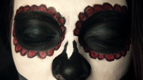 Close-up of opening eyes of a girl with makeup for holiday of Santa Muerte. Theme of costumes and transformation for holiday of Halloween. Traditional skull makeup for the day of the dead celebration
