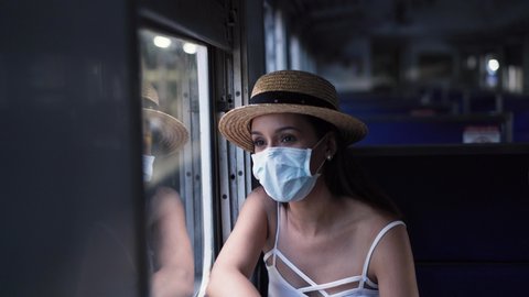 Young brunette woman traveling in Thailand on train during Coronavirus pandemic. 20s Hispanic girl in a protective mask wearing summer sleeveless clothes and backpack in Asia.