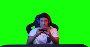 Excited professional young asian male cyber sport gamer in headset holding remote ontrollers concentrated playing in online video game over green screen background. POV monitor screen view.