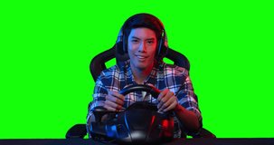 POV Excited young asian pro cybersport gamer in headset sitting in the racing seat simulator cockpit with steering wheel and playing in car racing online video game over green screen background.