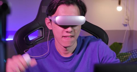 Excited young asian teen gamer wearing virtual reality glasses and holding controllers having fun enjoy playing motion sensing interaction vr game in colourful UV lighting living room at home.  Video de stock