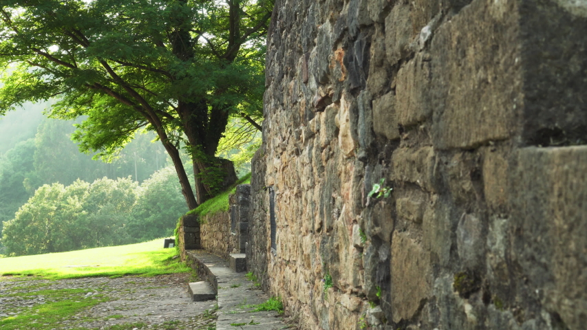 Stone wall on a lawn with green grass in a forest on a hill. Natural stone. Sunny summer day. Beautiful sunny landscape