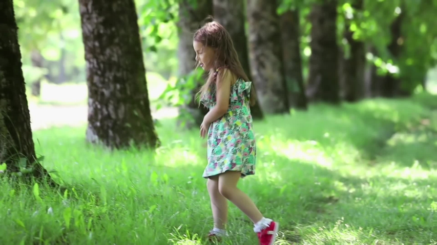 Little girl crouches in the green grass and examines a small bug