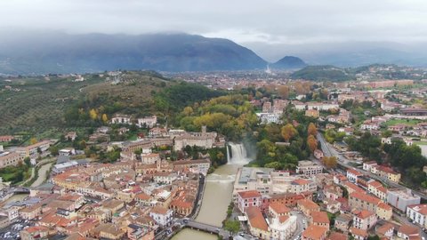 Picturesque view of downtown Lazio, Isola del Liri waterfall, fortified palace and mountains in background on cloudy day, Italy, aerial