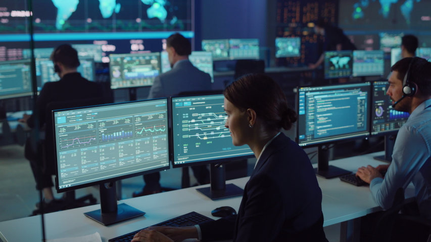 Team of Professional Computer Data Science Engineers Work on Desktops with Screens Showing Charts, Graphs, Infographics, Technical Business Data and Statistics. Dark Control and Monitoring Room.