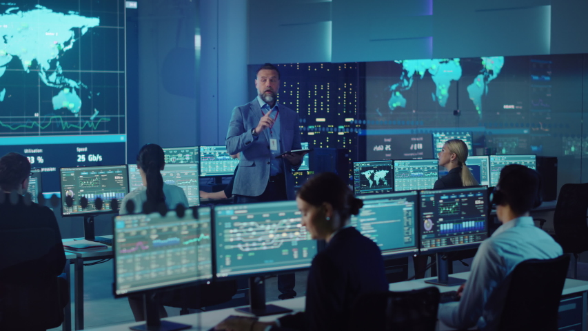 Senior Male Project Leader with Tablet Computer Makes an Announcement to the Team of Data Science Engineers. Telecommunications Control Monitoring Room with a Global Map on Big Screen. | Shutterstock HD Video #1055506856