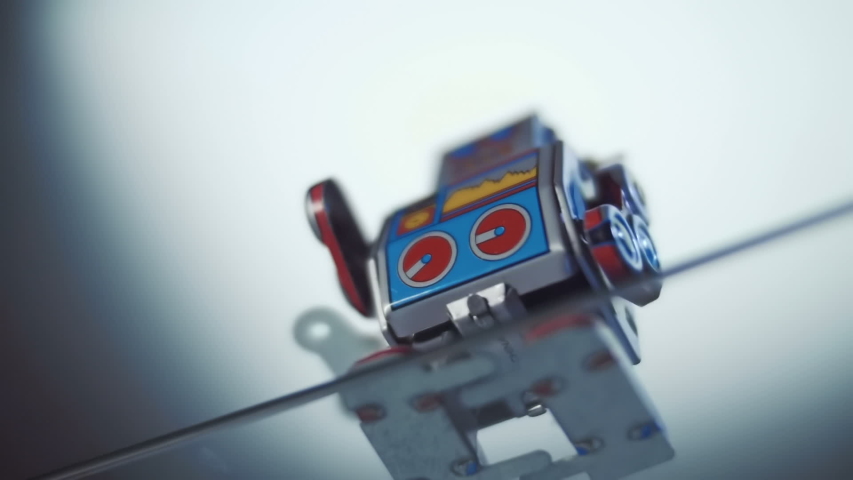 An antique cheerful colorful metal clockwork robot move on the glass surface and falls from the edge down.  