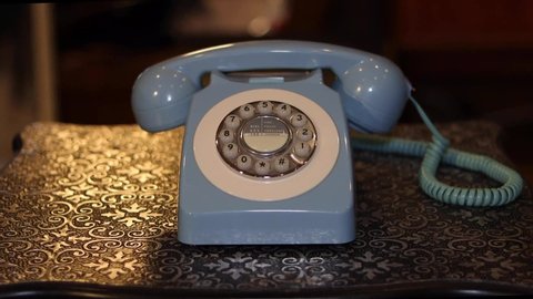 An old telephone on a metal table background with a male picking up the phone and hanging it up.