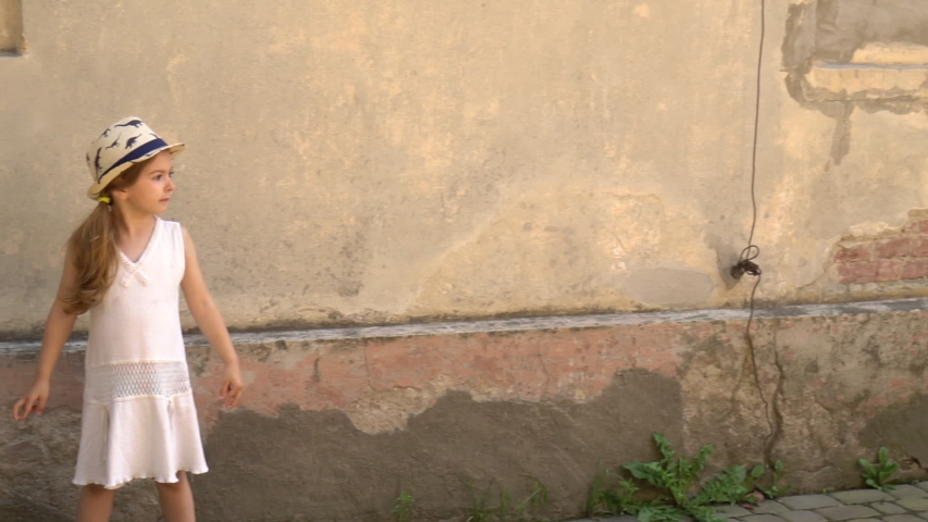 Little girl plays by the old wall. Tourist child after pandemic.