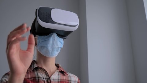 Slow motion: portrait of woman wearing medical face mask, virtual reality headset, looking around, moving hands at home. VR, self isolation, quarantine, COVID 19, coronavirus, technology concept Video de stock