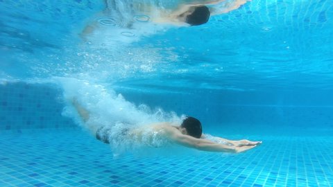 Asian young fit male diver swimmer in swimwear swimming in pool. Seen from on ground then underwater while man jumping and dive into the water. Sport workout and exercise for good health concept.
