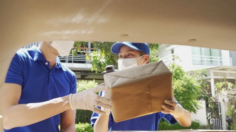 Asian deliver man and woman wearing face mask in blue uniform searching and handling parcel box, carrying by female worker give to costumer. Postman and express grocery delivery service during covid19