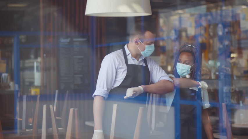 View through window of waiters in facial mask and gloves greeting each other touching elbows in cafe. Restaurant staff chatting before opening. Small business, teamwork and epidemic concept Royalty-Free Stock Footage #1055518727