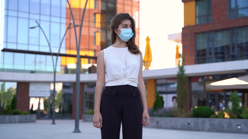 Girl student wearing protective coronavirus medical mask on city street, skyscraper on background.Concept of health and safety life, N1H1 coronavirus, virus protection, pandemic in world | Shutterstock HD Video #1055527259