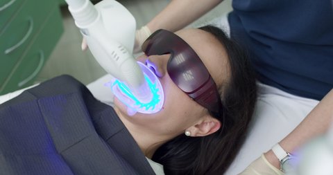 Teeth whitening procedure. Powerful light source is directed at patient's mouth to speed up the process. Dentist stomatologist whitening teeth for patient in medicine dental clinic with lamp.