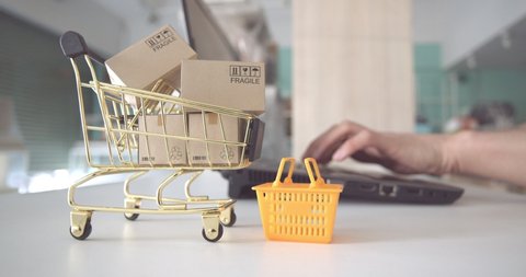 Online shopping / ecommerce and delivery service concept : Box or cartons in a shopping cart or trolley, buyer or customer uses a laptop to order things from retailer sites and pay by online payment
