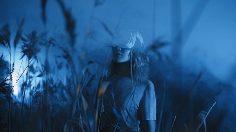 Cute girl wearing VR headset or helmet in blue neon light. Young woman uses virtual reality device outdoors. Digital art exhibition or online event stream using extended reality technology, concept 庫存影片