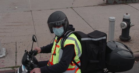 Masked food delivery man transports orders to customer's homes during the COVID-19 pandemic - everyday hero, essential worker