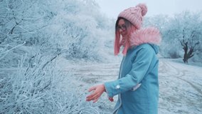 Joyful happy young beautiful woman tenderly touches branches winter trees. Fun touches nose snow tree. Girl admire, enjoy beauty snowy frosty nature. Pink long hair, warm hat, fashionable blue jacket 