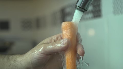 Cleaning a carrot on the kitchen faucet in slow motion.