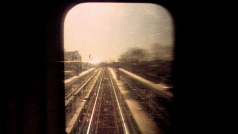 2019: Retro looking footage filmed on Super 8 on the New York City subway looking out through subway window at tracks and passing train with apartments and graffiti in the distance