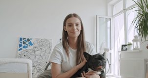 Smiling young woman blogger vlogger influencer sit at home with black french bulldog. Girl speaking looking at camera talking making video chat, conference call lifestyle blog vlog, webcam view