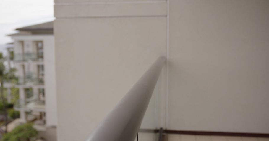 Caucasian middle aged male sets hands down on hotel balcony railing as he waits patiently. tropical setting. 