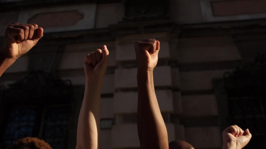 Raised fists against the backdrop of a city wall. People are chanting slogans. The protest against racism. Protests in the USA | Shutterstock HD Video #1055557382