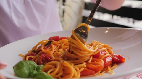 Closeup woman eat pasta in italian cuisine restaurant spinning spaghetti on a fork beautiful dish layout with tomatoes and basil